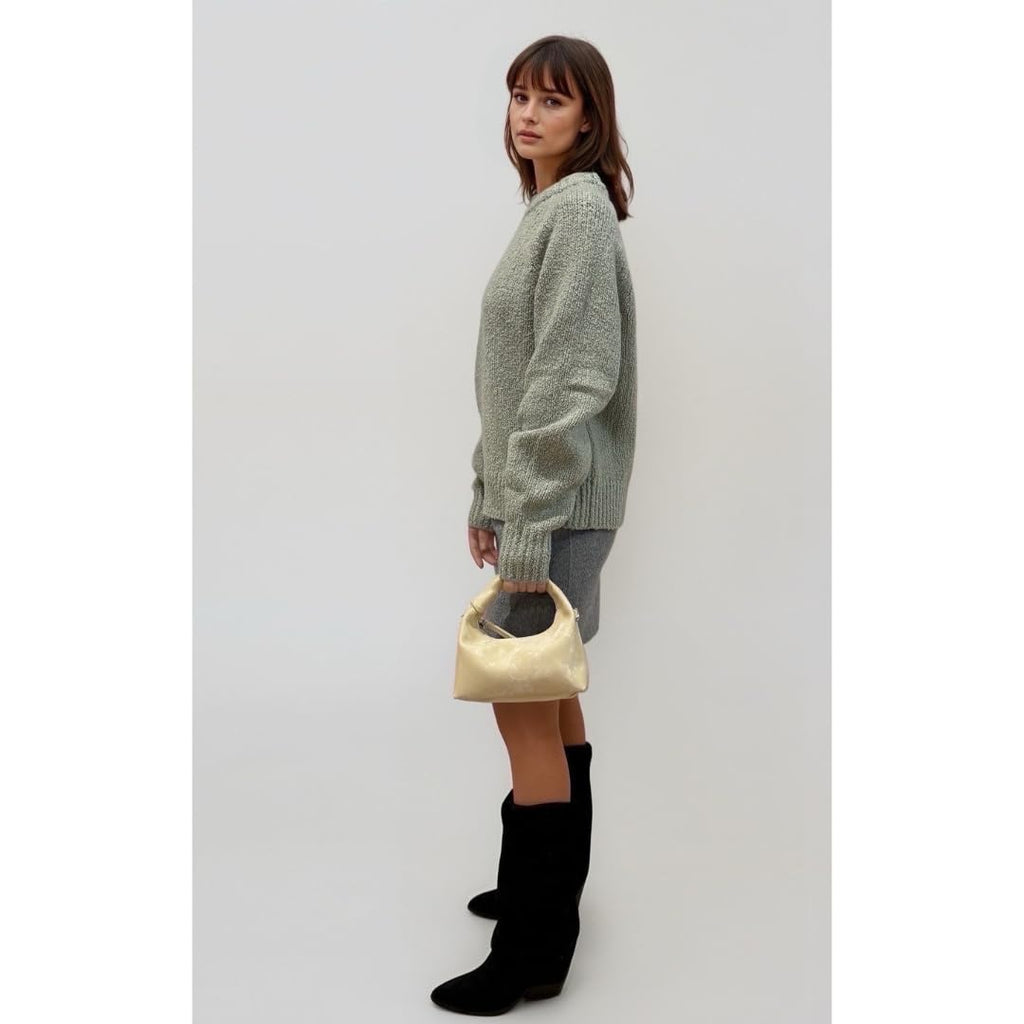 Woman holding a golden yellow handbag wearing a green sweater and black boots on a white background