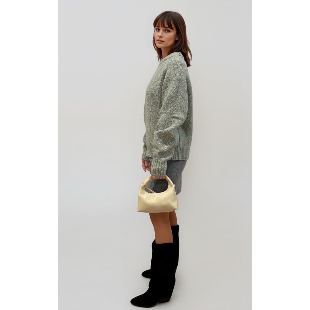 Woman holding a golden yellow handbag wearing a green sweater and black boots on a white background